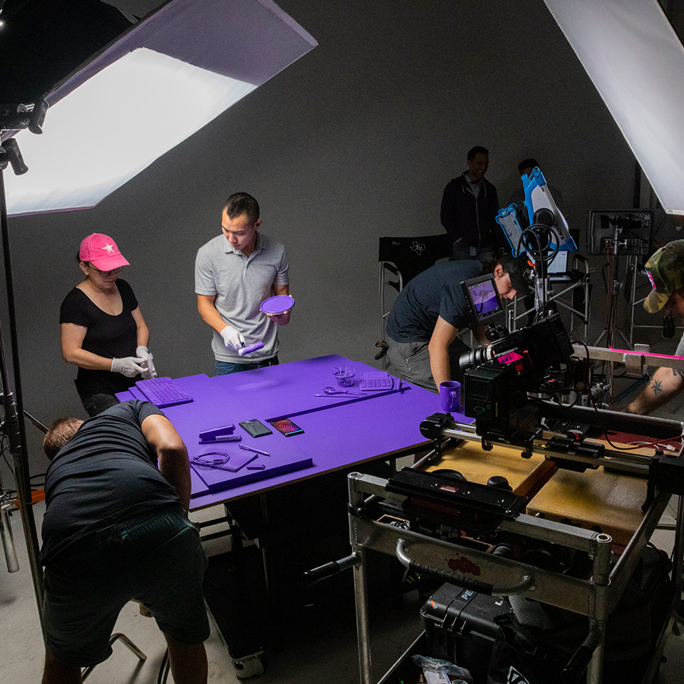 A behind the scenes pohoto of commercial studio shoot. Props are painted bright purple and surrounded by a camera and many lights.
