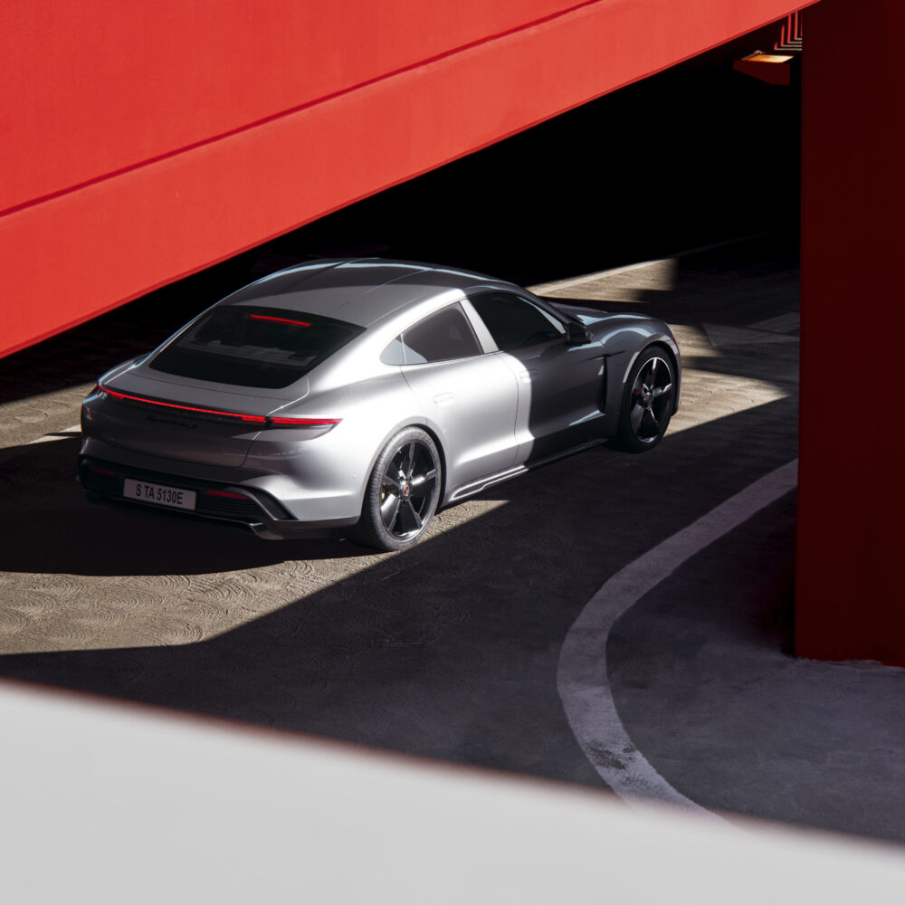 A render of a Porsche Taycan Turbo in a bright-red painted parking garage.