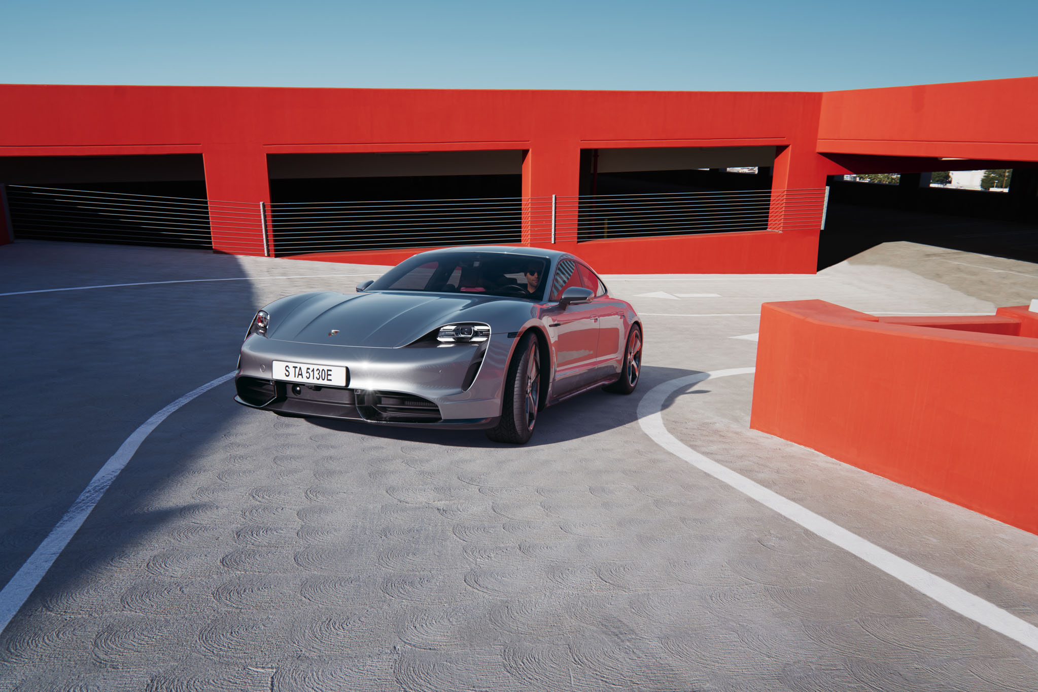 A render of a Porshe Taycan Turbo in a bright red-painted parking garage.