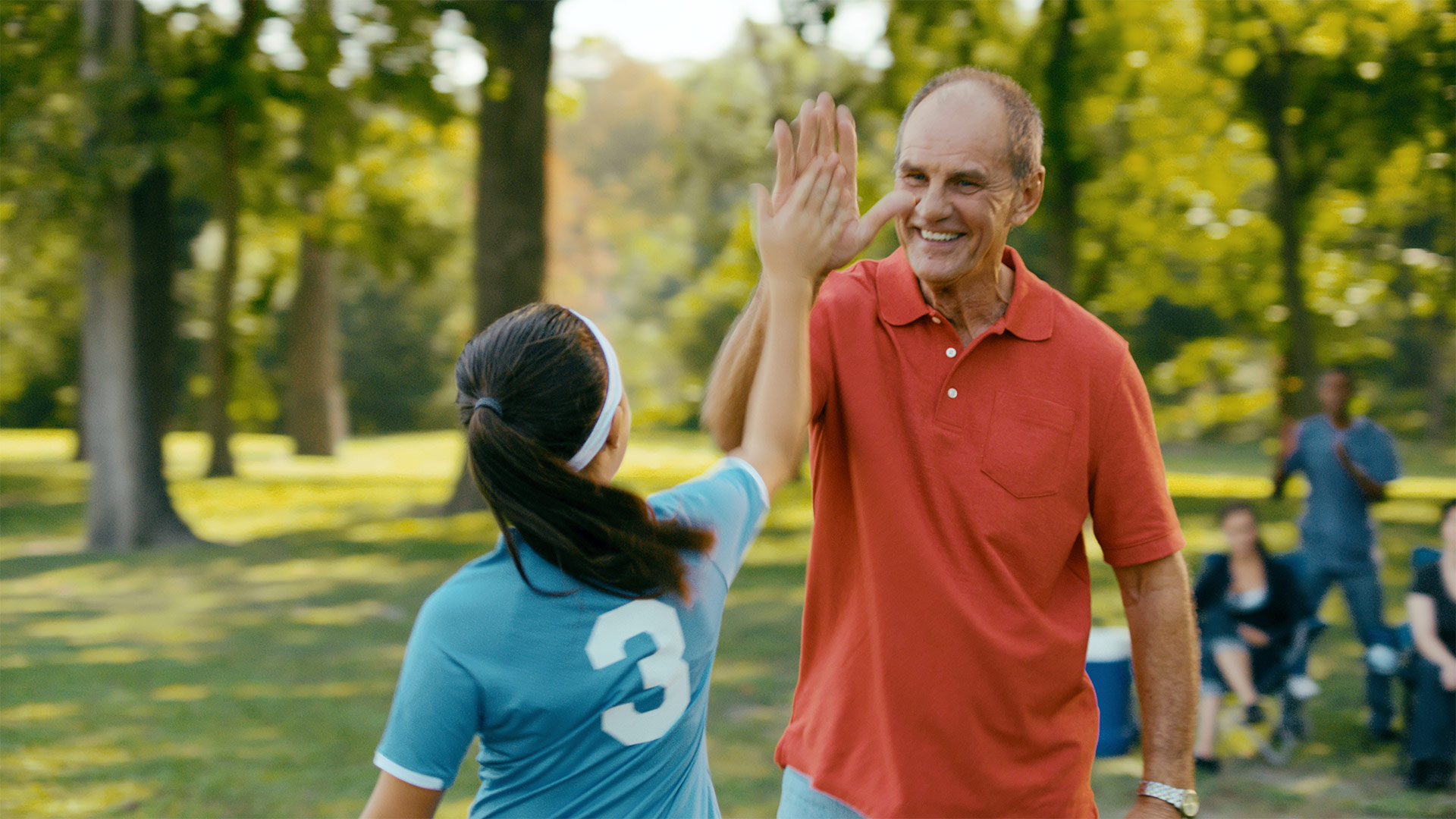 A man high-fiving a young woman playing soccer.