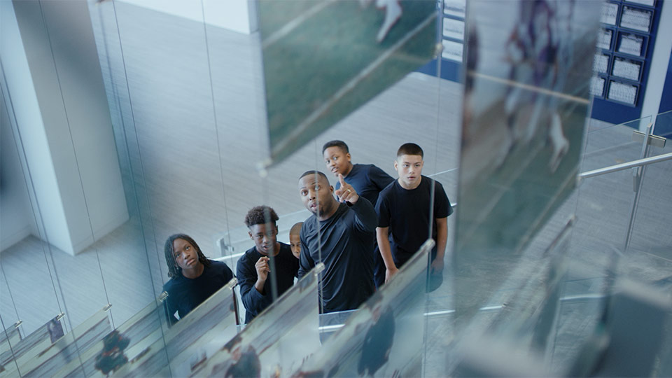 A man points to a photo in the Dallas Cowboys training stadium as a group of kids look on.