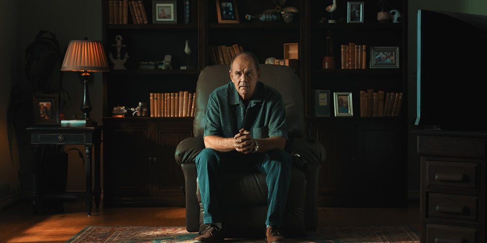 A man talking to the camera while sitting in a armchair.