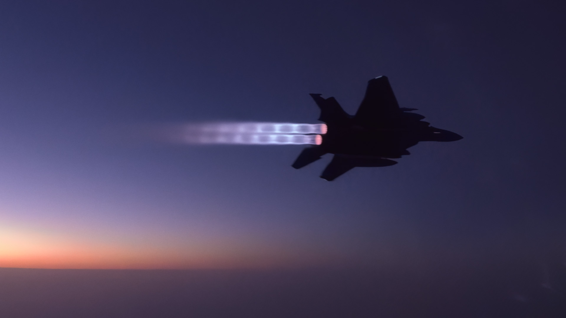 A F-15E flying at dusk with afterburners on